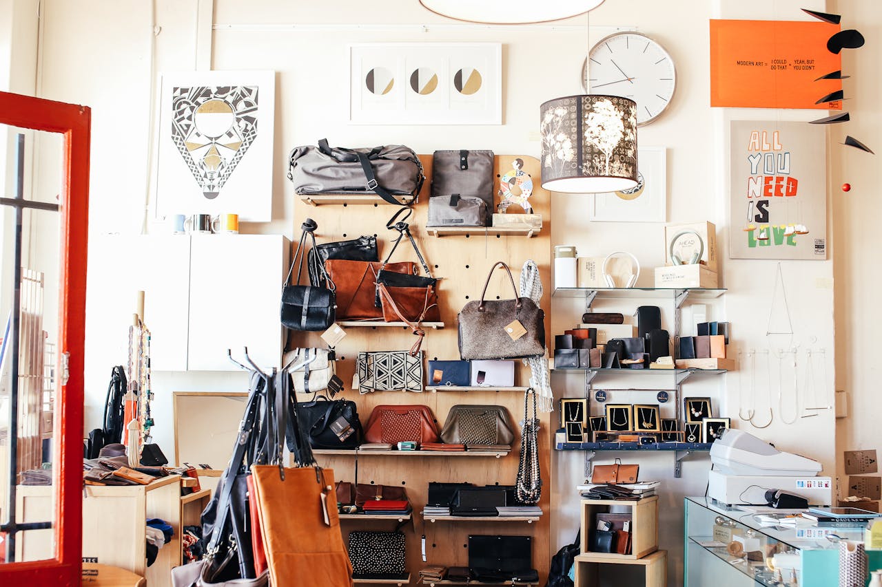 Abundance of stylish bags placed on shelves near wall with various goods and decorations in modern light shop with cashbox